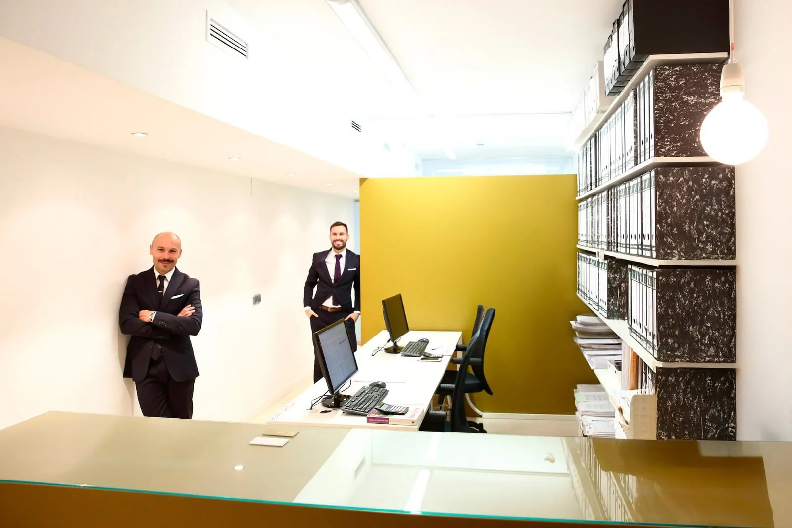 Diego y Rubén Villar Aretio en el despacho, junto a la pared ocre y la estantería de archivadores